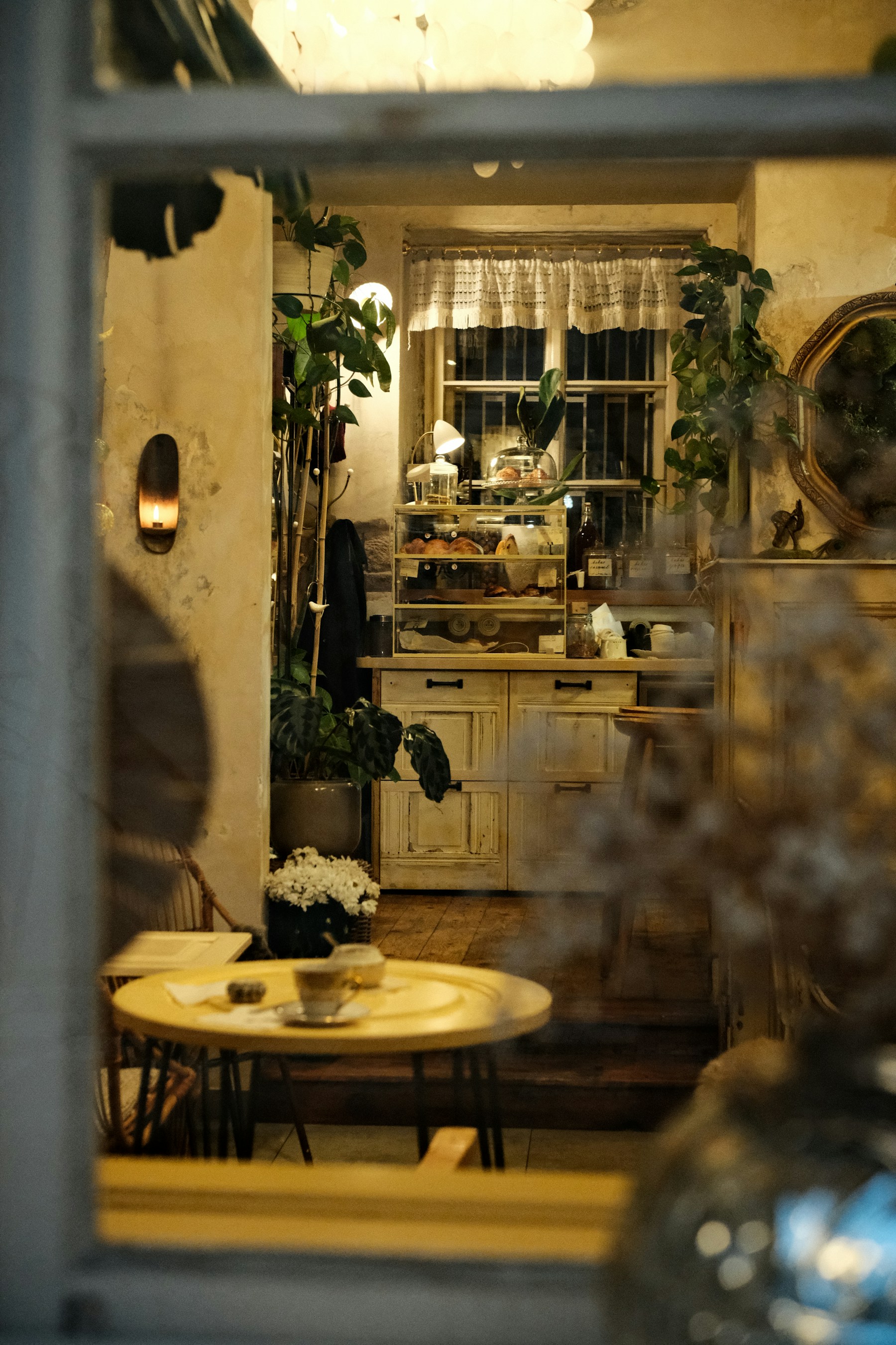 A cozy café with warm lighting, leafy plants, and coffee waiting at a small table